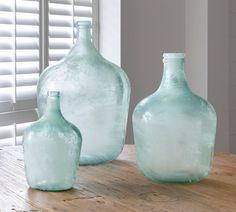 three glass vases sitting on top of a wooden table next to a white window