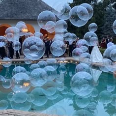 bubbles floating in the air next to a swimming pool with people standing around and looking at them