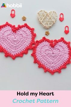 two crocheted hearts are next to each other on a white surface with the words hold my heart written in red