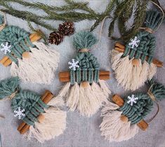 four christmas ornaments made out of yarn and wood sticks, with pine cones on top