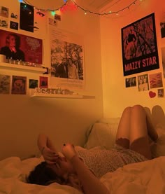 a woman laying on top of a bed in a bedroom with posters above her head