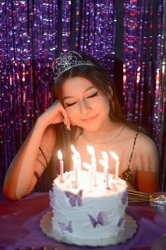 a young woman sitting in front of a cake with lit candles on it and wearing a tiara