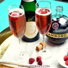 two glasses of champagne and raspberries sit on a table next to a bottle