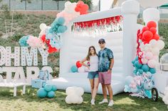 a man and woman standing in front of an inflatable birthday party arch with balloons