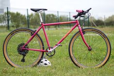 a pink bike parked in the grass with a soccer ball on it's front tire