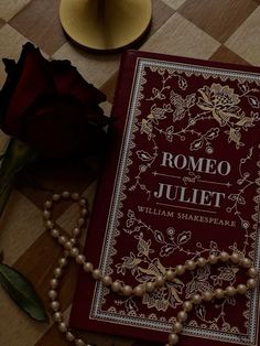 a red book sitting on top of a table next to a rose and a beaded necklace