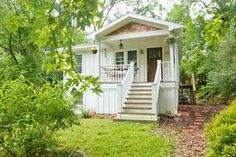 a small white house in the woods with stairs leading up to it's front door