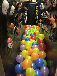 many balloons are lined up on the floor in front of black walls and plastic heads