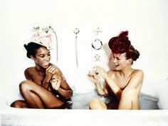 two women sitting in a bathtub with soap on their faces and one holding a rose