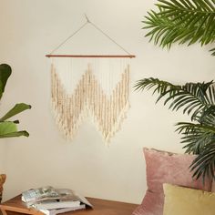 a wooden table topped with a plant next to a hanging beaded wall decoration on a white wall