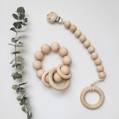 a wooden bead necklace and ring on a white surface next to a plant with leaves