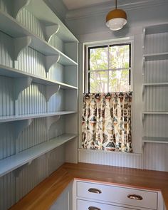 an empty room with white shelves and a window in the corner that has a curtain on it