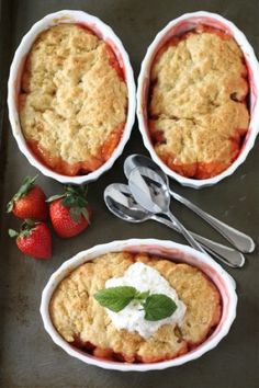 three desserts in white dishes with strawberries and spoons next to them on a table