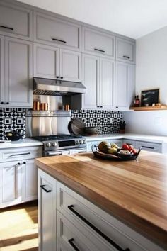 a kitchen with white cabinets and wooden counter tops, along with a bowl of fruit on the island