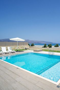 an empty swimming pool with lounge chairs and umbrellas on the deck overlooking the ocean