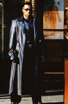 a man in a black coat and sunglasses standing on the street