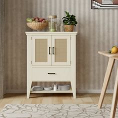 a white cabinet sitting next to a table with food on top of it and a potted plant in the corner