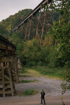 a man standing on the side of a road next to a train track and bridge