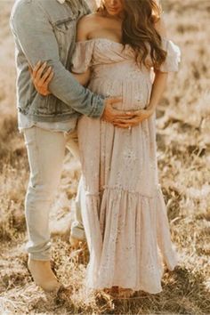 a pregnant couple standing in the middle of a field with their arms around each other