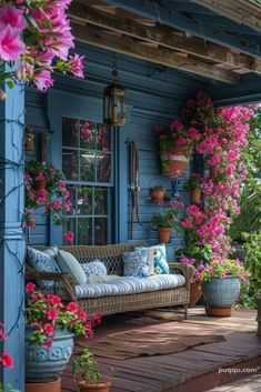 a porch covered in lots of flowers next to a blue building with potted plants