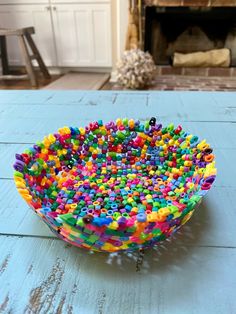 a bowl filled with lots of colorful beads on top of a wooden table next to a fire place