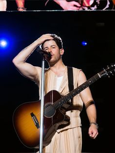 a man holding a guitar while standing next to a microphone on top of a stage