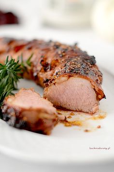 a white plate topped with meat covered in sauce and garnished with green herbs