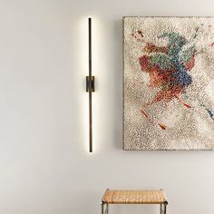 a painting is hanging on the wall next to a stool and light fixture in a white room