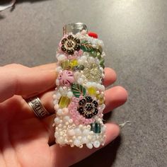 a hand holding a cell phone case made out of bead and glass beads with flowers on it