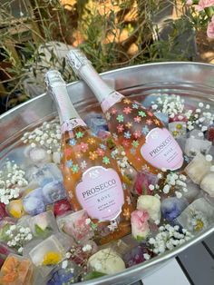 two bottles of champagne sitting on top of ice cubes in a metal bowl filled with flowers