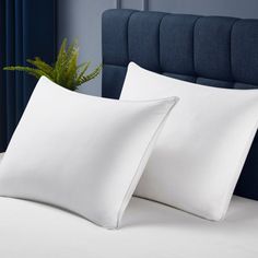 two white pillows sitting on top of a bed next to a plant in a pot