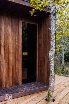 a tree in front of a wooden building with its door open and the entrance to it