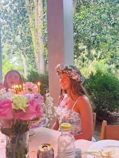 two women sitting at a table with flowers in front of them and candles on the table