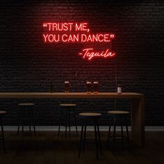 a neon sign that says trust me, you can dance tequila on a table in front of a brick wall