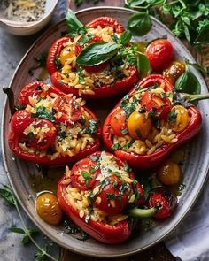 four stuffed red peppers on a plate with herbs and seasoning in the bowl next to them