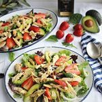 two plates of salad with strawberries and avocado on the side next to a bottle of wine