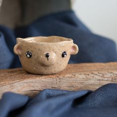 a small ceramic bear bowl sitting on top of a wooden table next to blue cloth