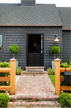 the front door of a gray house with wooden fence and planters on either side