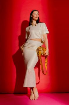 a woman standing in front of a red wall with her hands on her hips wearing a white skirt and crop top