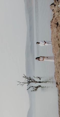 two people standing next to each other on the beach with snow and water in the background