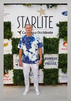 a man standing in front of a starlite sign wearing white pants and a blue shirt