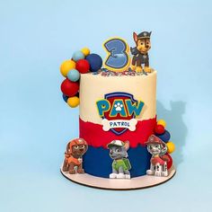 a birthday cake with paw patrol characters on top and balloons around the base, in front of a blue background