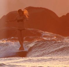 a woman riding a surfboard on top of a wave in the ocean at sunset