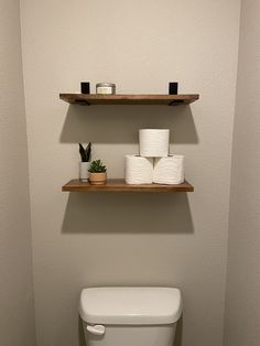 a toilet with two shelves above it and some rolls of toilet paper on the shelf