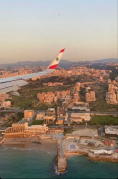 an airplane wing flying over a city next to the ocean with buildings in the background