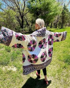 a woman standing in the grass with her arms spread out and wearing a colorful blanket