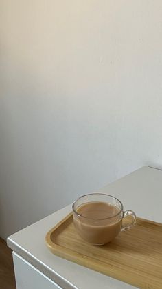 a cup of coffee sitting on top of a wooden tray next to a white wall