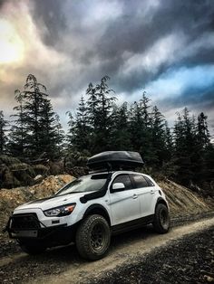 a white suv is parked on the side of a dirt road with trees in the background