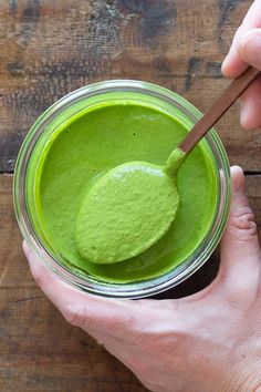 a person holding a spoon in a jar filled with green liquid