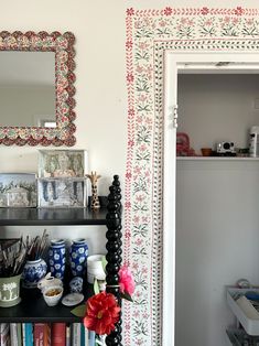 there is a mirror on the wall above a shelf with dishes and cups in it